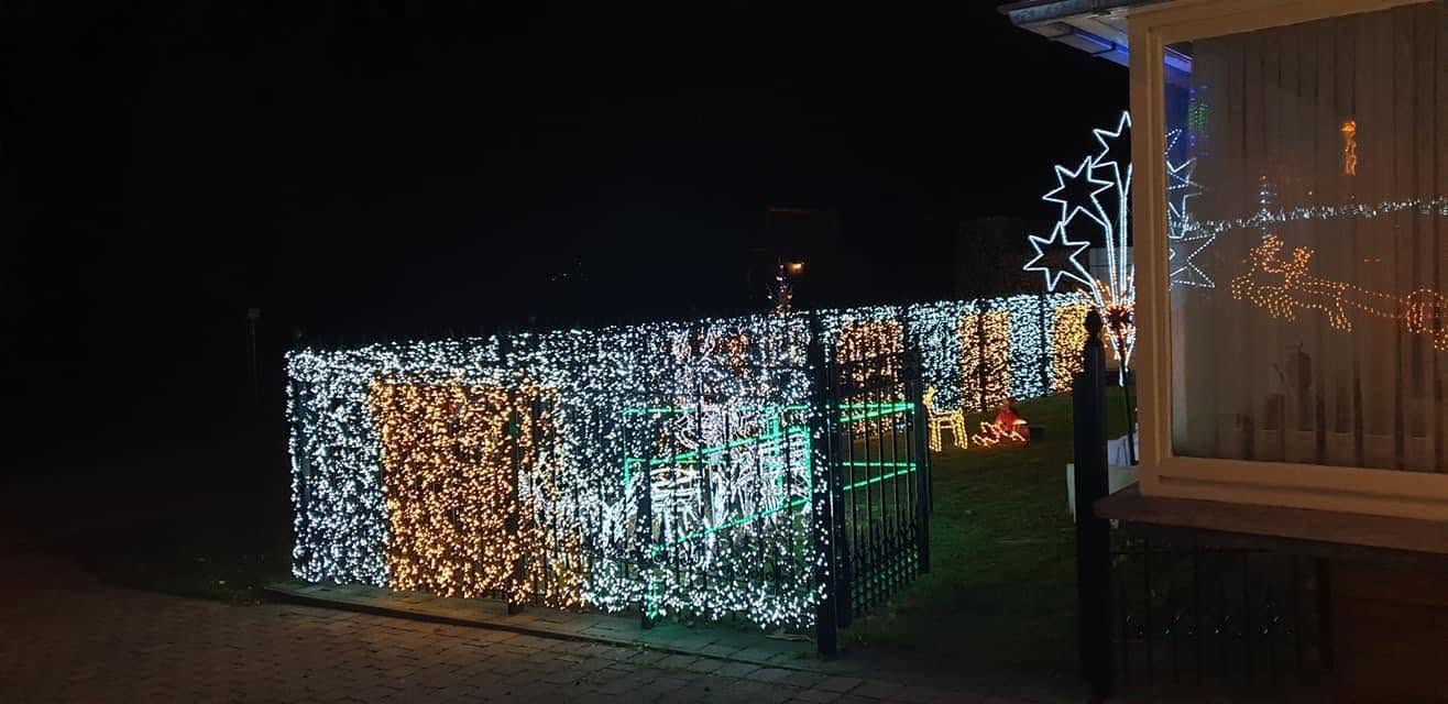 De ingang van de tuin met witte en gouden lichtslingers en verlichte sterren